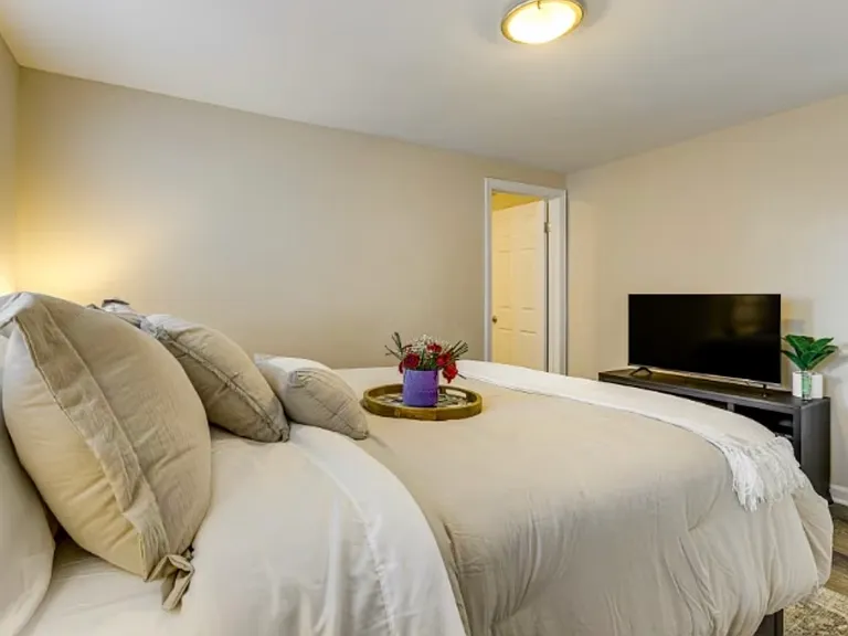 Stylish master suite with two bedside tables, flat-screen TV, and plenty of natural light _ fully furnished for comfort and convenience.