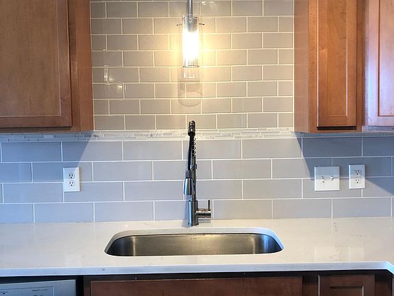 The kitchen features a large, single basin inlay sink with extendable faucet, beneath a custom backsplash of subway tiles with artisanal touch