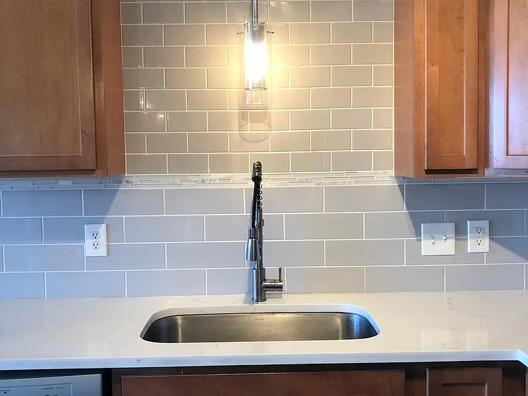 The kitchen features a large, single basin inlay sink with extendable faucet, beneath a custom backsplash of subway tiles with artisanal touch