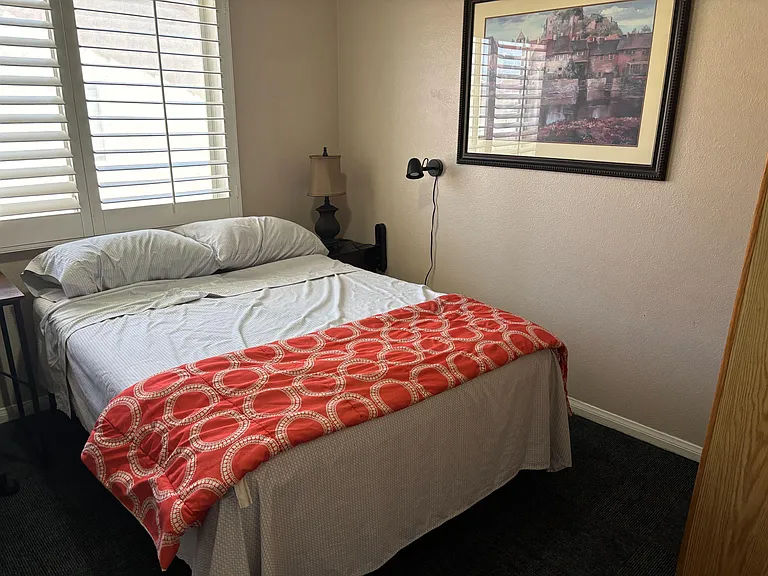 Furnished bedroom with a full-size bed, nightstand lighting, and window shutters for adjustable light and privacy.