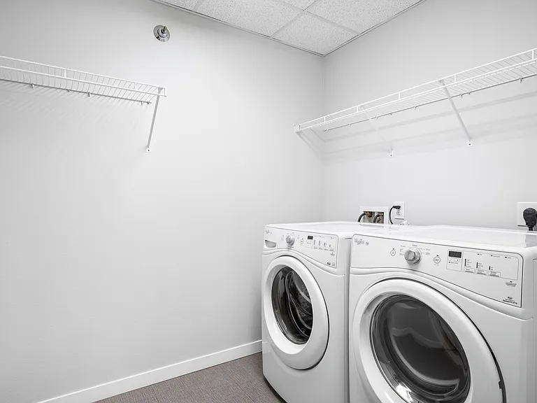 Modern laundry room featuring state-of-the-art washing and drying machines with convenient shelving for storage. Modern laundry room featuring state-of-the-art washing and drying machines with convenient shelving for storage.