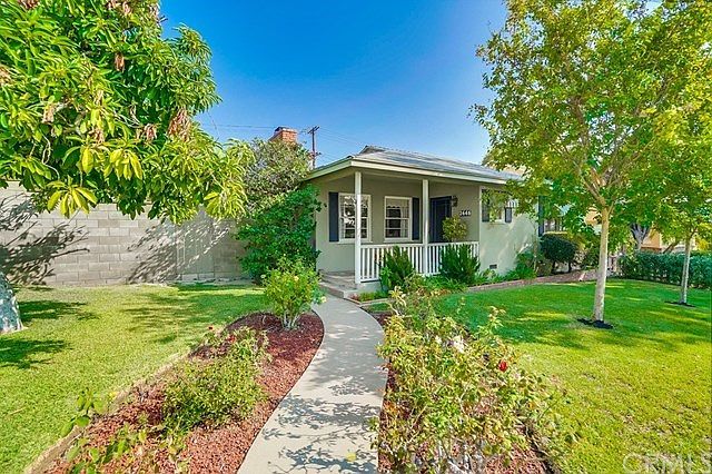 Beautifully landscaped with walkway bordered with rose bushes, avacado tree, lush lawn, mature flowering plants.