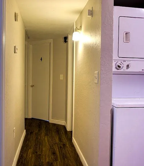 Hallway with wood-look flooring and wall lighting, plus convenient in-home stacked laundry closet near bedrooms.