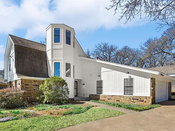 View of front of property with stone siding, an attached garage, concrete driveway, roof with shingles, and a gambrel roof