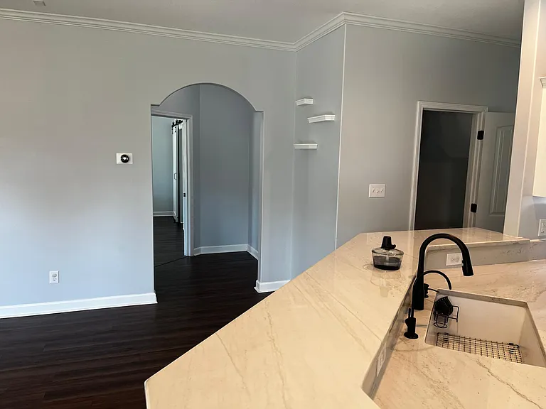 Large kitchen island overlooking the open living area, with arched entryways and decorative corner shelving.