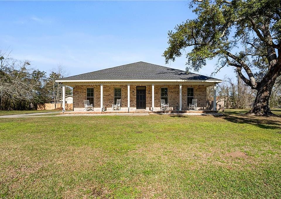 View of front of home featuring covered porch, a front lawn, a shingled roof, and brick siding