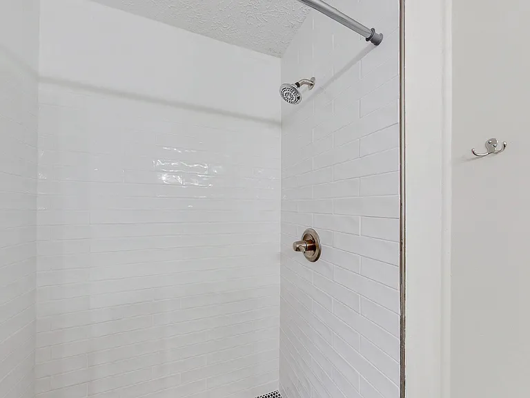 Clean tub/shower combo with white tile surround, curved shower rod, and updated shower fixtures for daily convenience.