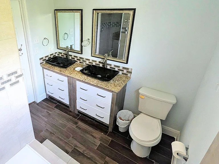 Bathroom with double-sink vanity, granite countertop, framed mirrors, and tiled shower surround with updated flooring.