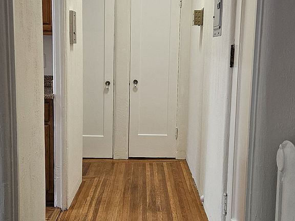 Interior hallway to #2 viewed from main room. An entrance to kitchen at left, front door to unit #2 at right, closet doors at rear, door to bathroom (not shown) to left of closet doors