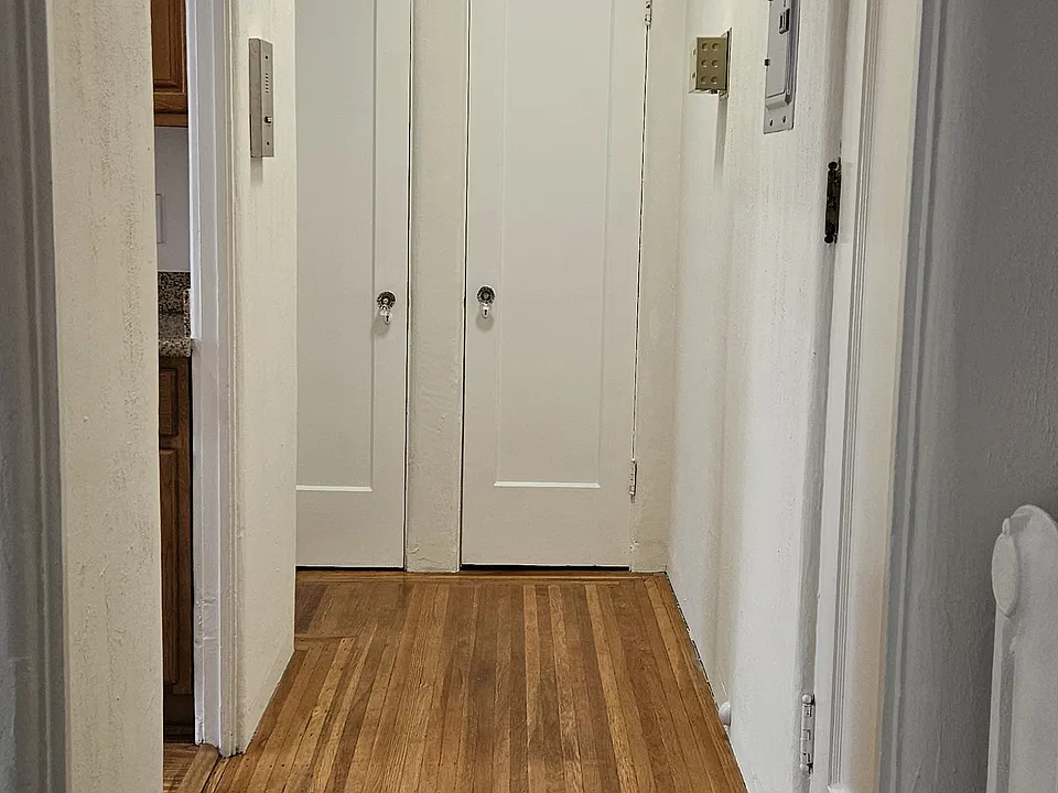 Interior hallway to #2 viewed from main room. An entrance to kitchen at left, front door to unit #2 at right, closet doors at rear, door to bathroom (not shown) to left of closet doors