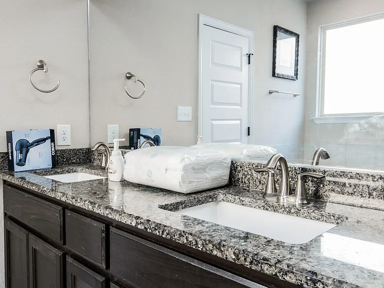 Bathroom vanity with dual sinks, granite countertop, large mirror, and window for natural light and easy daily routines.