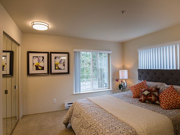 A large bedroom with a queen sized bed, nightstands, mirrored closets, and two large windows