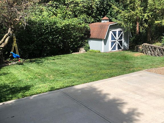 Flat, grass back yard with shed, perennial plants, and fire pit surrounded by a pea gravel pad.