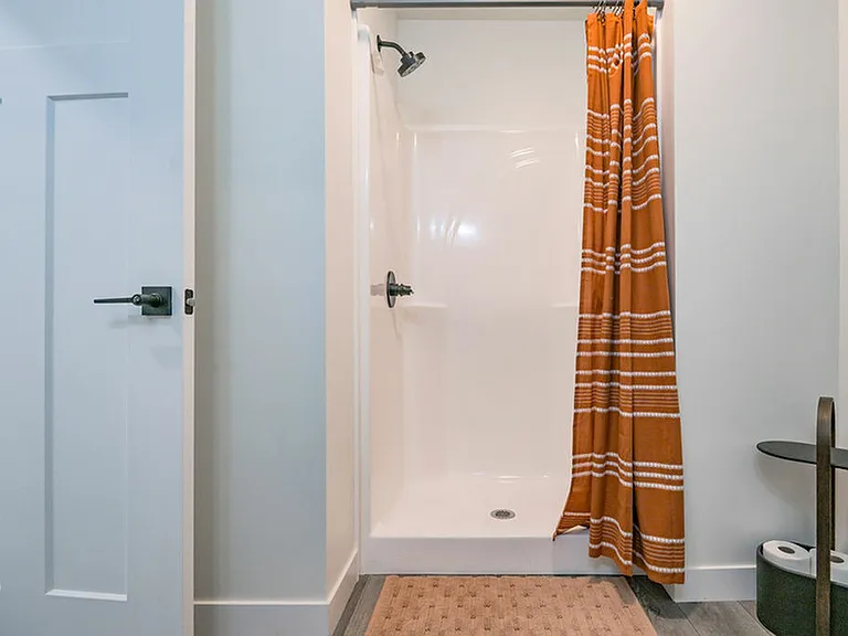 Bright bathroom with modern shower and stylish orange striped curtain, offering a refreshing space.