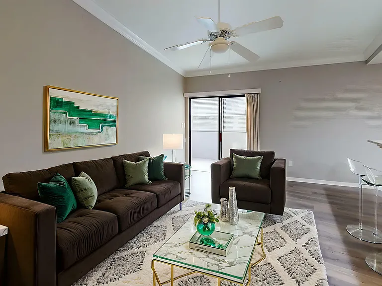 Elegant living room with a plush dark sofa, matching armchair, and chic glass coffee table on a patterned rug, enhanced by modern decor and abundant natural light.
