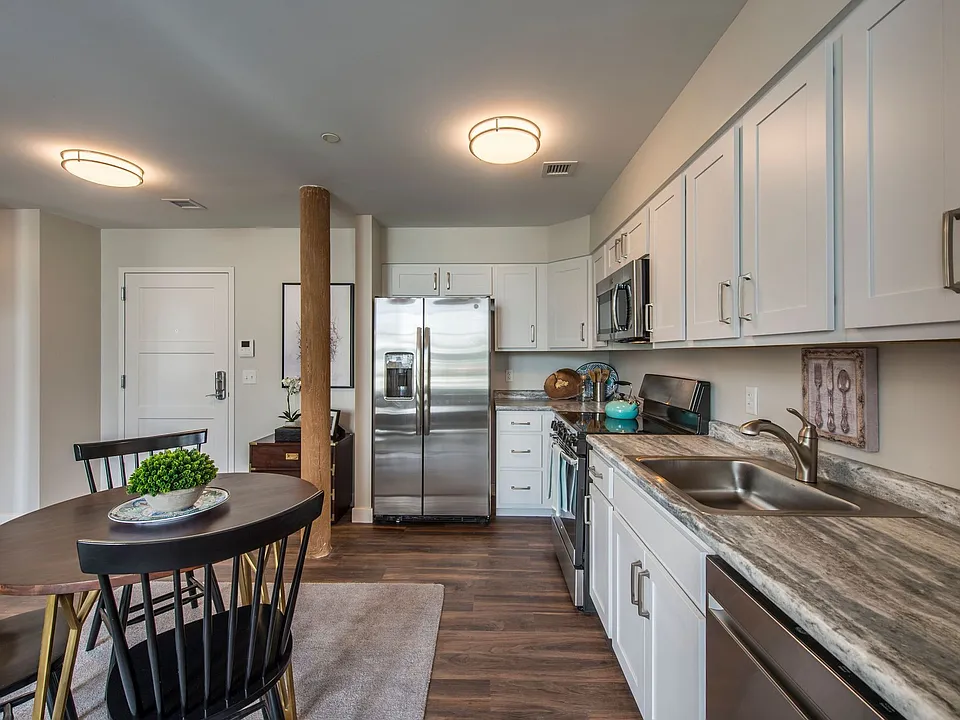Kitchen And Dining Room With Faux Quartz Counters, White Cabinets, Stainless Appliances, Wood Plank.