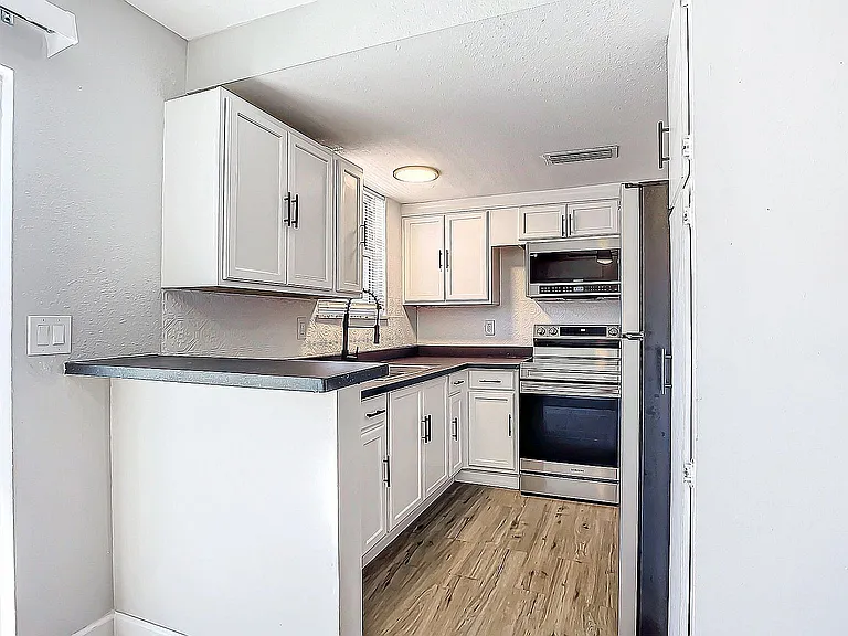 Modern kitchen with sleek white cabinetry, stainless steel appliances, and elegant wood flooring, offering a stylish and functional cooking space.