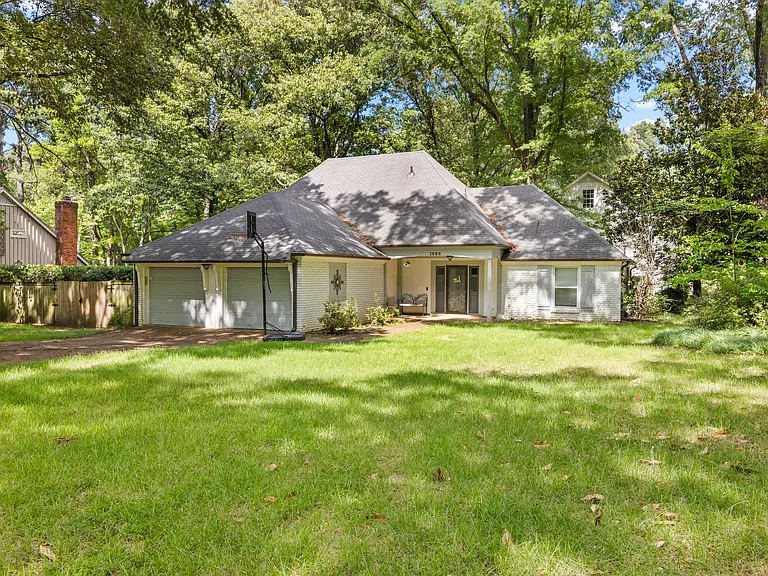 Beautiful wide-angle view of the home set beneath a canopy of mature trees with a manicured sweeping front lawn.
