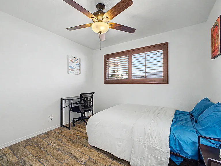 Furnished bedroom with a full bed, dedicated desk space, and a ceiling fan, plus a window with wood blinds.