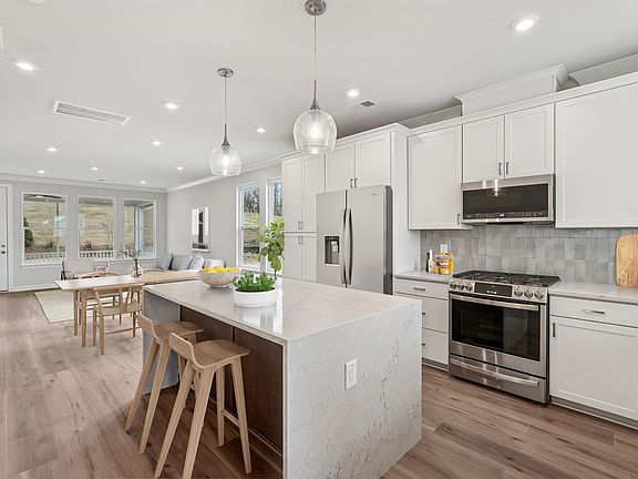 A modern, open-concept kitchen with white cabinets, stainless steel appliances, and a large island w
