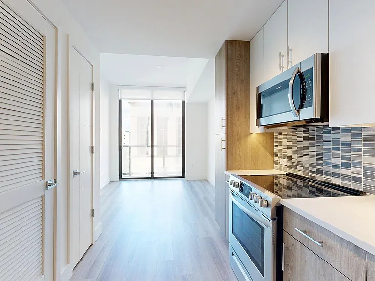 Apartment Kitchen with Stainless Steel Appliances, Dining and Living Room with Wood Style Flooring.