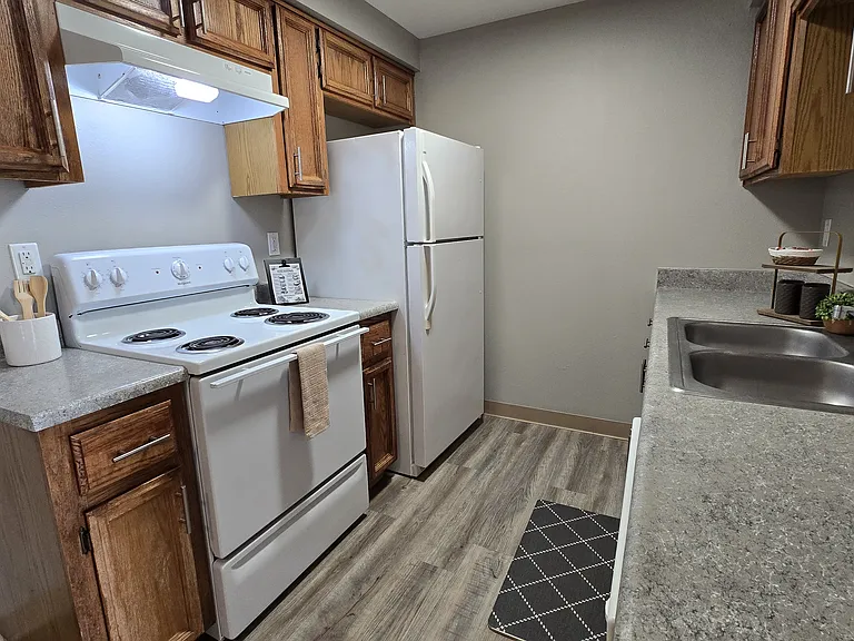 Clean, functional kitchen with warm wood cabinetry, ample counter space, and white appliances. Features a double sink and an efficient layout, ideal for everyday cooking.