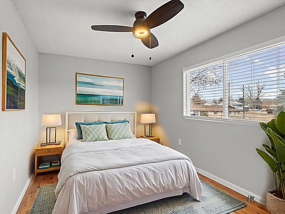 Bright bedroom with elegant decor, featuring a cozy bed, artistic wall paintings, and a large window offering serene views.