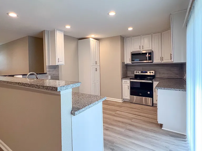Updated kitchen with stainless steel appliances, white cabinetry, and granite countertops.