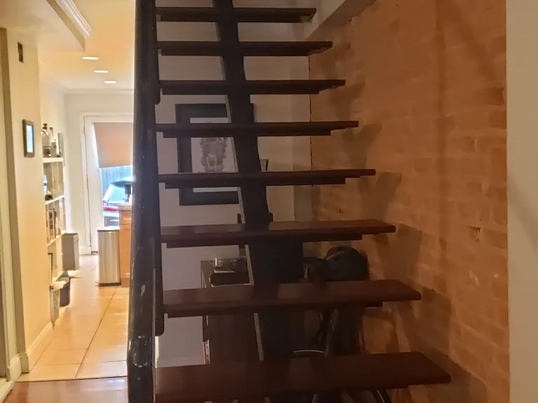 Floating staircase at first floor showing view to second floor hallway and galley kitchen behind staircase.