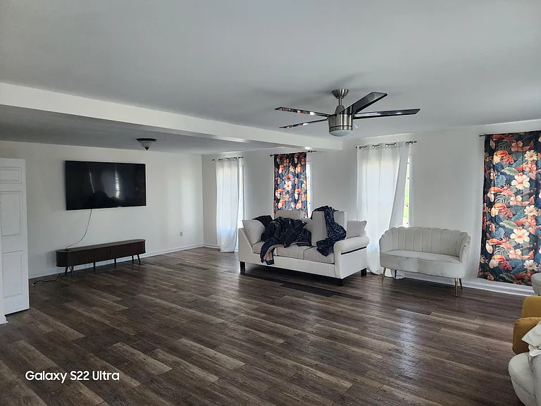 Spacious living room with wide-plank flooring, ceiling fan, and multiple windows for natural light plus a TV mount wall.