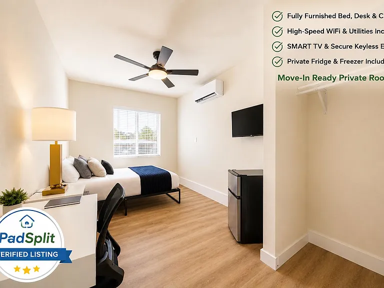 Private furnished bedroom with work desk, ceiling fan, wall-mounted TV, mini fridge, and an open closet area.