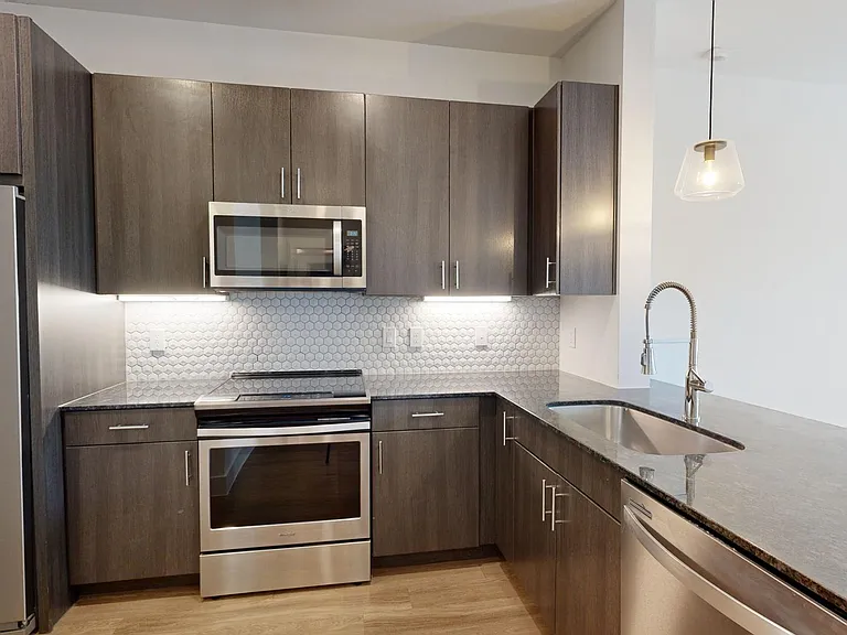 Apartment kitchen with stainless steel appliances, granite countertops, and wood-style flooring.