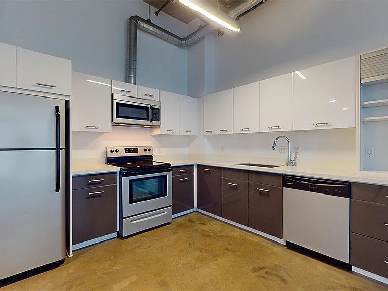 Apartment kitchen with stainless steel appliances, quartz countertops and polished-concrete flooring.