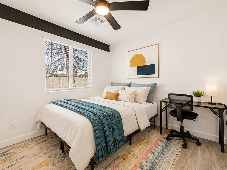 Well-sized bedroom with a large window, ceiling fan, and space for a dedicated desk or study area.