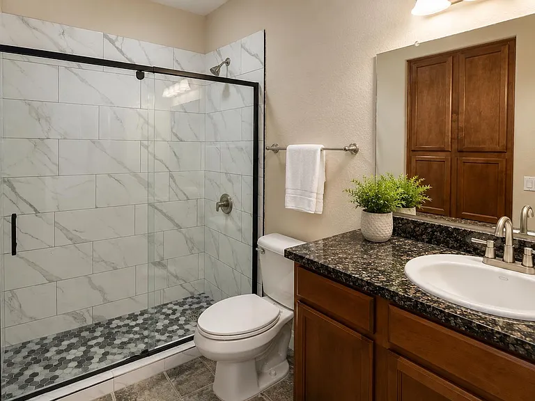 Updated bathroom with a glass-enclosed tiled shower, granite vanity, and ample cabinet storage for daily essentials.