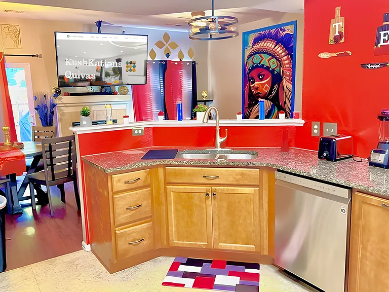 The vibrant red kitchen, with warm wood tones, offers an inviting atmosphere enhanced by a large flat-screen TV & a captivating Native American painting.