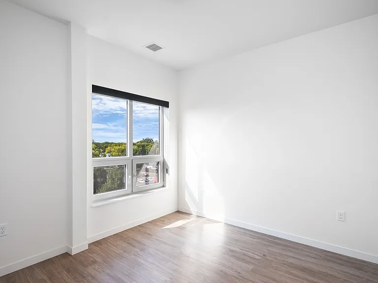 Bright, sunlit room featuring sleek wood flooring and a large window with a scenic view, perfect for a modern, cozy apartment. Bright, sunlit room featuring sleek wood flooring and a large window with a scenic view, perfect for a modern, cozy apartment.