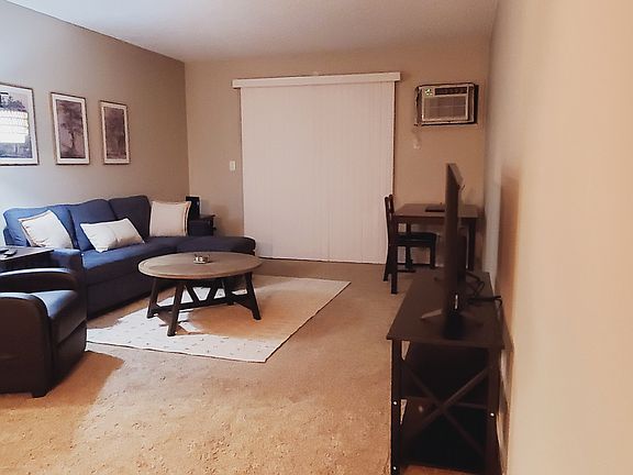 Living room with couch, chaise, recliner, writing table, end tables, floor lamp, coffee table, and smart TV.