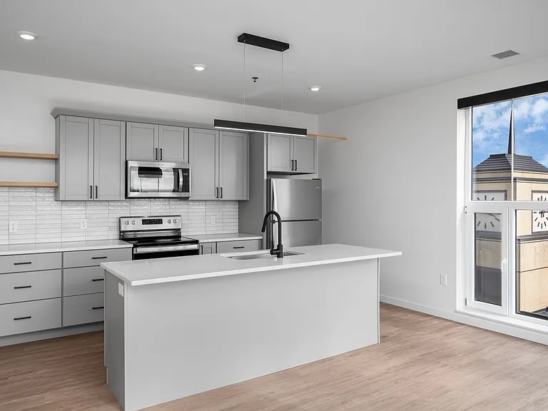 Bright, contemporary kitchen with sleek gray cabinetry, modern appliances, and a large island, featuring a panoramic window view of urban architecture. Bright, contemporary kitchen with sleek gray cabinetry, modern appliances, and a large island, featurin