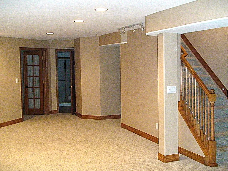 Basement stairway view and view of basement area leading to bathroom and bedroom doors at back of pic.