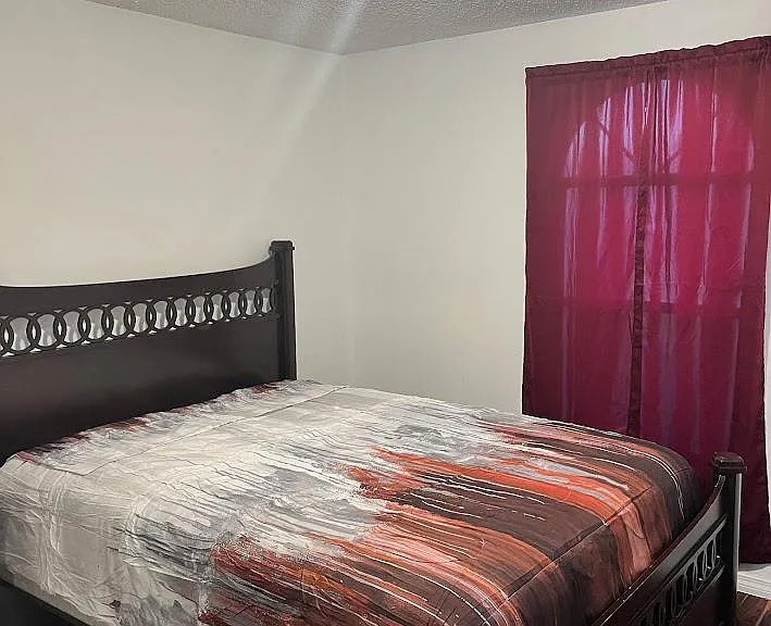 Furnished bedroom featuring a full-size bed, overhead lighting, and a window with curtains for added privacy.
