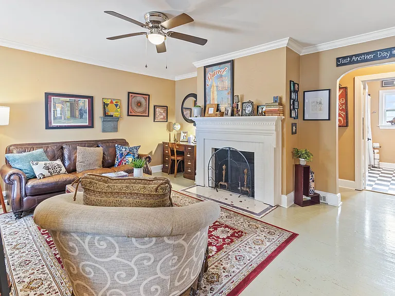 Cozy living room at Hunsucker's Place near Downtown Greensboro, featuring a comfortable leather couch, a functional writing desk, and an open-concept design connecting to the dining room with a piano and the fully equipped kitchen_perfect for relaxation