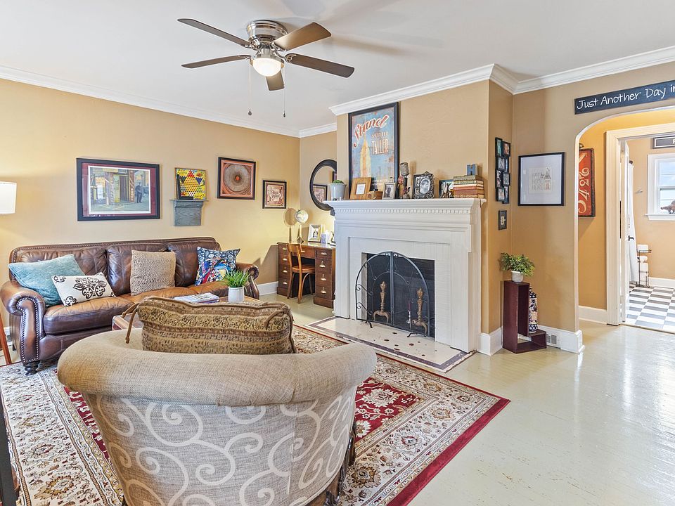 Cozy living room at Hunsucker's Place near Downtown Greensboro, featuring a comfortable leather couch, a functional writing desk, and an open-concept design connecting to the dining room with a piano and the fully equipped kitchen_perfect for relaxation