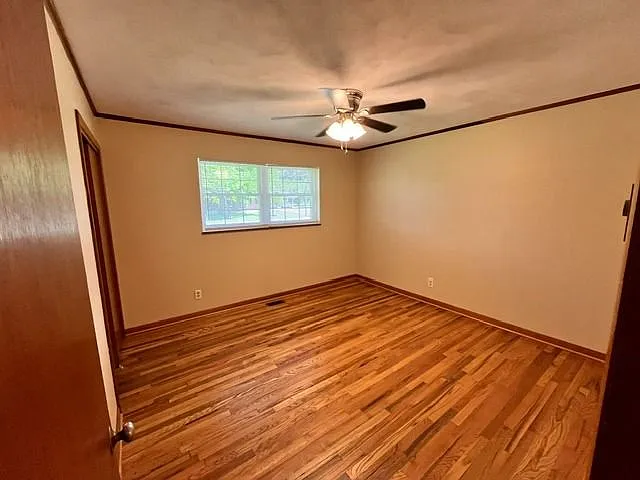 Cozy bedroom featuring stunning hardwood floors, neutral paint tones, and a large window that brings in natural light. The room offers a clean, open layout with ample wall space for furniture placement and decor. Includes a modern ceiling fan with lightin
