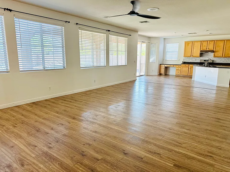 Spacious open-concept family room with abundant natural light, wood-look flooring, an updated ceiling fan, and seamless flow into the kitchen.