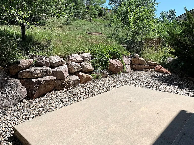 Patio/backyard nestled against a hillside bordered by stone
