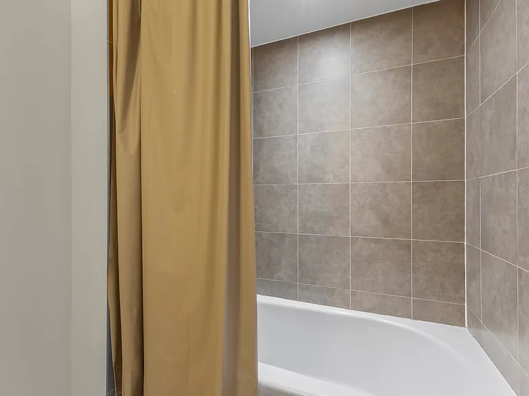 Enjoy a quiet soak in the full-size tub, finished with elegant floor-to-ceiling tiling for a polished, modern look.