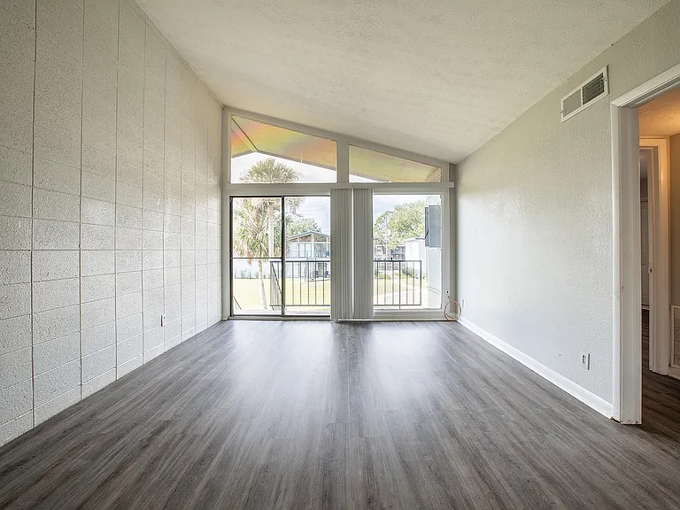 Bright, open living space featuring large windows, vaulted ceiling, and sleek wood flooring, offering a seamless flow to outdoor views.