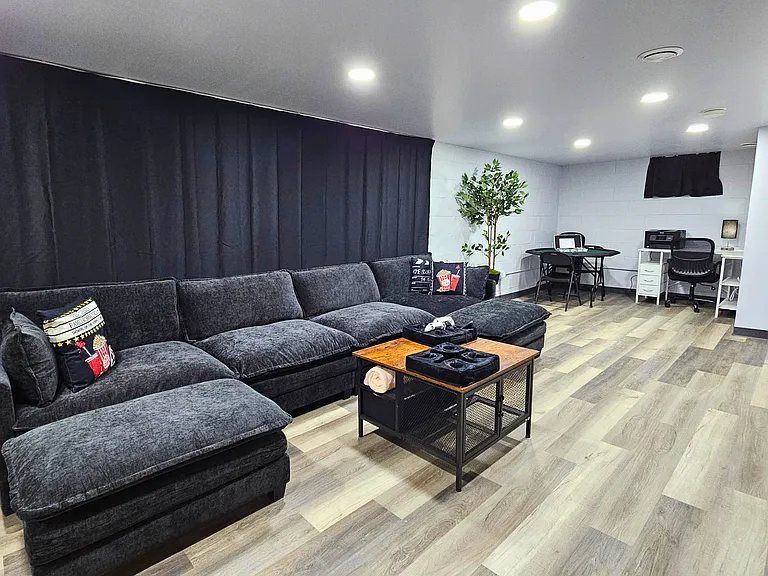 Lower level family room with large couch, large TV, desk in the corner and a variety of games along with an exercise bike