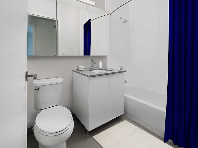 Renovated Package I bath with grey quartz countertop, white stone tub surround, and hard surface plank flooring